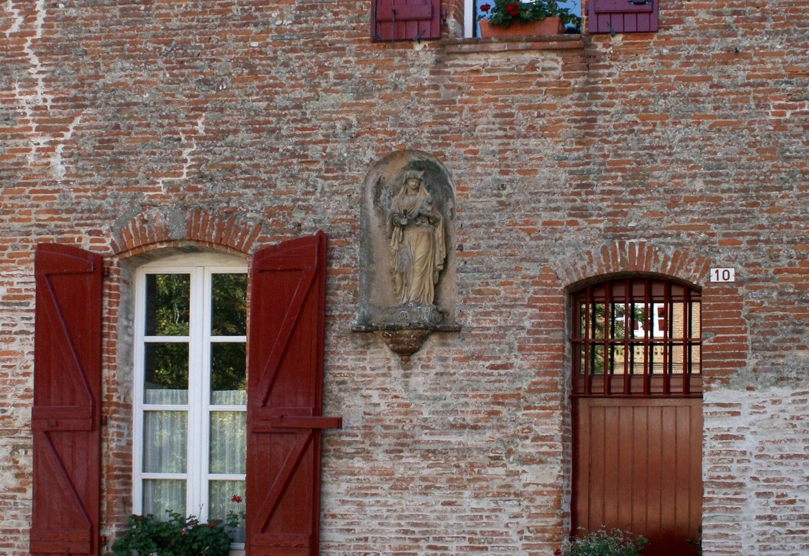 Fa�ade d'une maison ancienne en brique avec volets rouges dans le Lauragais